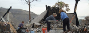 People sorting through a house destroyed by fire